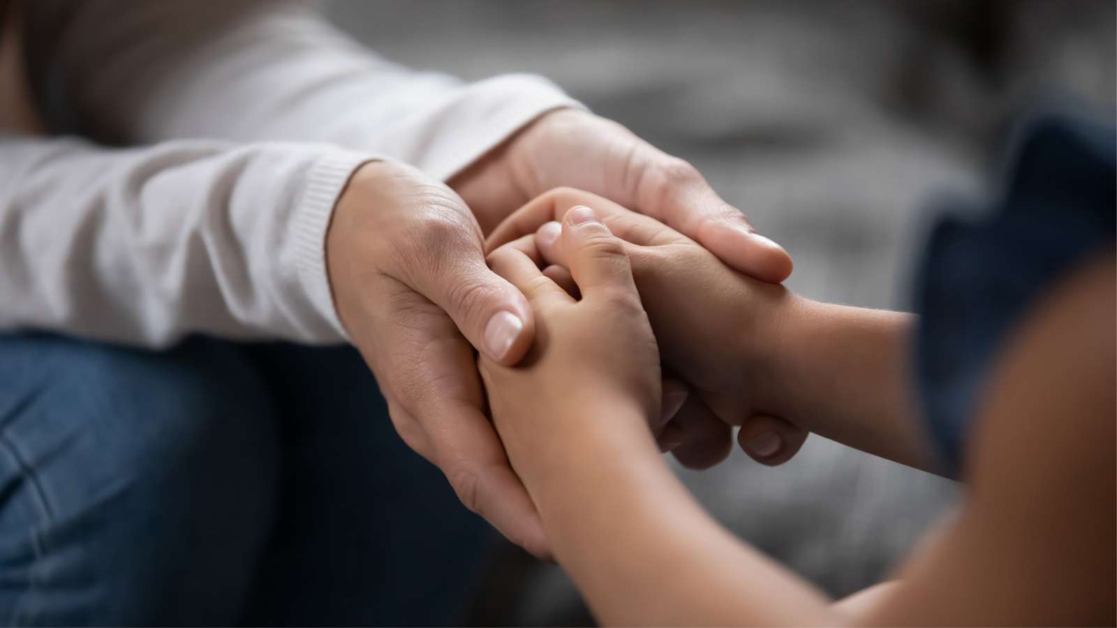Closeup of adult hands holding child hands in a comforting gesture.